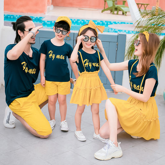 Family of four in matching dark blue short-sleeved tops with yellow text and yellow bottoms, posing outdoors. - Image 10