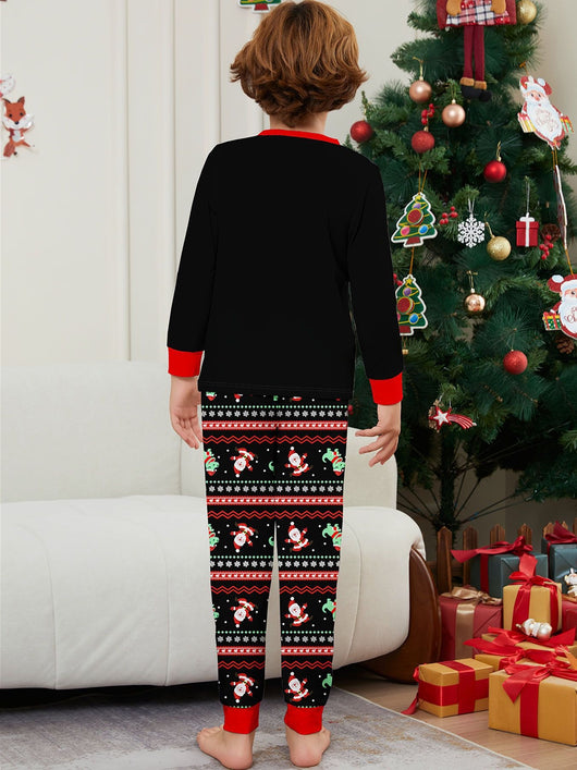 Man wearing black Christmas pajamas with a cartoon dinosaur, Santa Claus, and "Merry Christmas" text, standing by a decorated tree. - Image 10