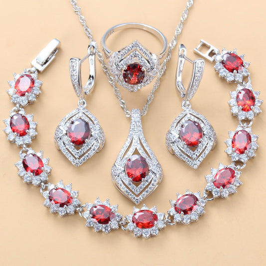 4-piece women's jewelry set with silver-tone necklace, ring, earrings, and bracelet, featuring red oval gemstones surrounded by clear accent stones.