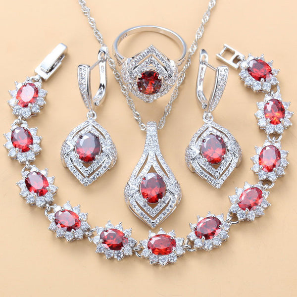 4-piece women's jewelry set with silver-tone necklace, ring, earrings, and bracelet, featuring red oval gemstones surrounded by clear accent stones.