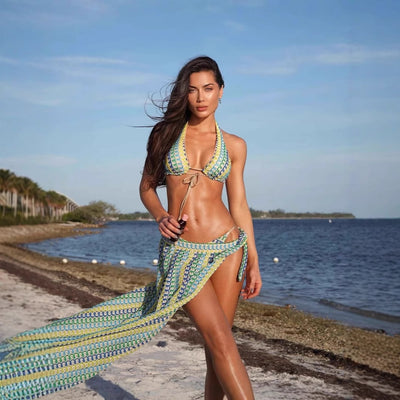 Woman in a blue, green, and yellow patterned halter bikini top and matching flowy sarong on a sunny beach.