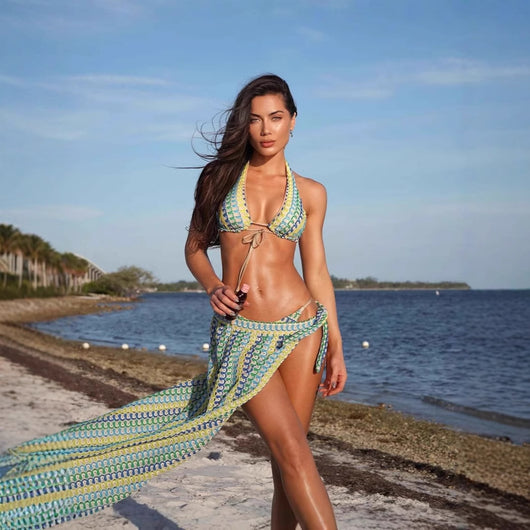 Woman in a blue, green, and yellow patterned halter bikini top and matching flowy sarong on a sunny beach.