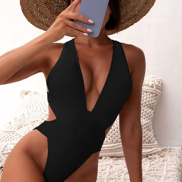 Woman in a black one-piece swimsuit with a deep V-neck and criss-cross waist cutouts, wearing a straw hat.