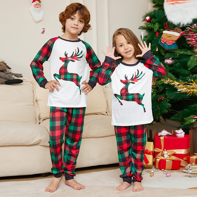 Two children in matching red and green plaid Christmas pajamas with a reindeer graphic, standing by a Christmas tree.