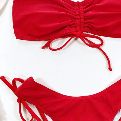 Red two-piece bikini with a strapless ruched bandeau top and matching side-tie bottoms, displayed on a white surface. - Image 8