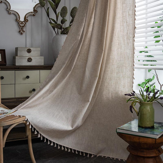 Light beige linen-like curtain with a brown embroidered border, draped over a white stool in a living room.