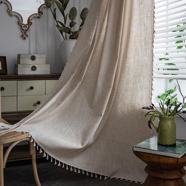Light beige linen-like curtain with a brown embroidered border, draped over a white stool in a living room.