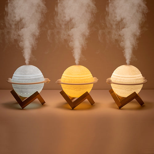Yellow planet-shaped humidifier with a wooden stand emitting mist, next to a dark blue celestial gift bag.
