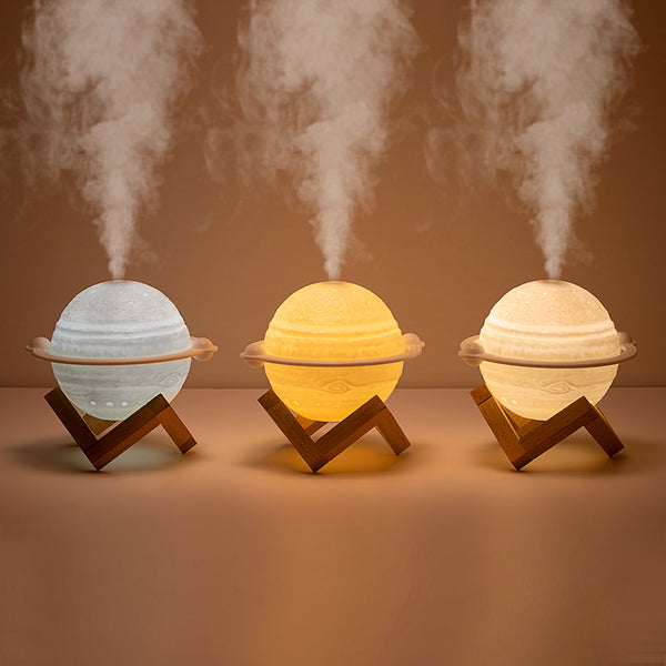 Yellow planet-shaped humidifier with a wooden stand emitting mist, next to a dark blue celestial gift bag.