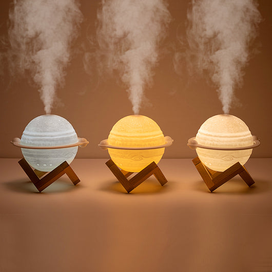 Yellow planet-shaped humidifier with a wooden stand emitting mist, next to a dark blue celestial gift bag.