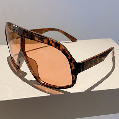 Oversized women's shield sunglasses with a tortoiseshell frame and brown-tinted lenses, held by a hand. - Image 20