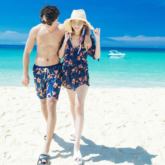 Man wearing navy blue swim shorts with a vibrant orange and green floral pattern, standing on a sunny beach.