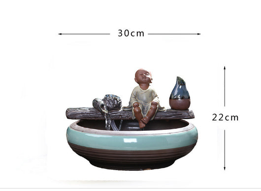 Ceramic flowing water ornament with a meditating monk figurine, small plant, and misting humidifier in a teal and brown bowl. - Image 8