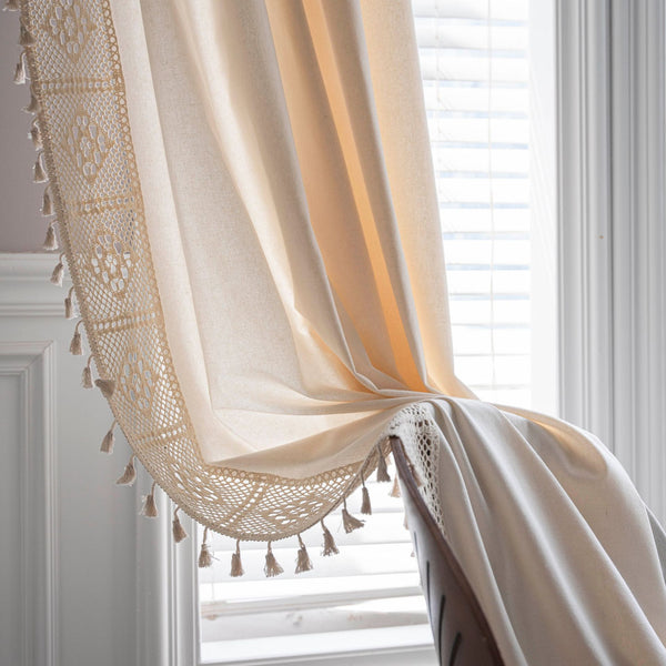 Close-up of a beige semi-transparent curtain with a delicate crochet lace trim and decorative tassels.