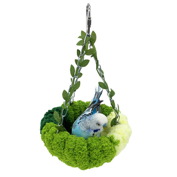 Small forest style plush bird hammock in green and yellow, hanging from a chain with artificial leaves.