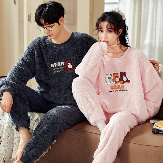 Couple wearing matching cream coral fleece pajamas with gray pants and bear embroidery, seated on a bed. - Image 9
