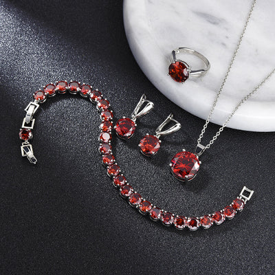 Four-piece jewelry set with silver-toned metal and round deep pink gemstones, including a necklace, bracelet, ring, and earrings.