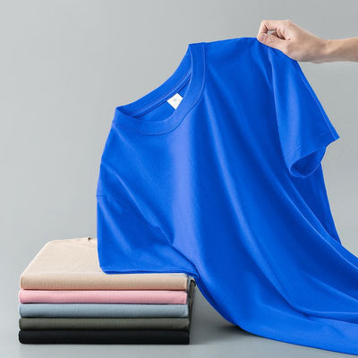 Light gray short-sleeve t-shirt with a round neck, held up to show its smooth fabric. A stack of folded t-shirts in various colors is visible in the background. - Image 8