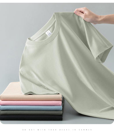 Light gray short-sleeve t-shirt with a round neck, held up to show its smooth fabric. A stack of folded t-shirts in various colors is visible in the background. - Image 17
