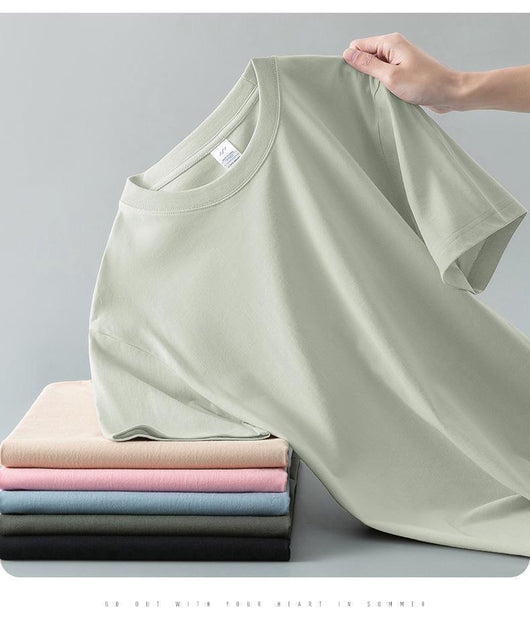 Light gray short-sleeve t-shirt with a round neck, held up to show its smooth fabric. A stack of folded t-shirts in various colors is visible in the background. - Image 17