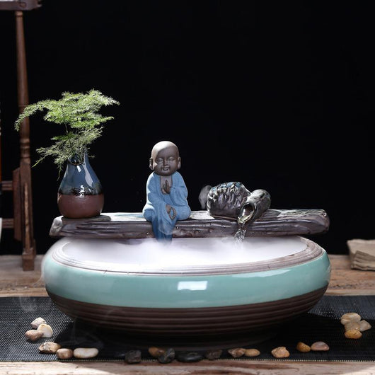Ceramic flowing water ornament with a meditating monk figurine, small plant, and misting humidifier in a teal and brown bowl. - Image 12
