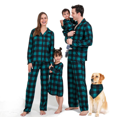 Family of four and dog wearing matching green and black plaid pajamas. Mother and father in two-piece sets, girl in dress, baby in two-piece, and dog in bandana