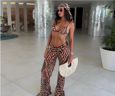 Woman in a brown and black animal print bikini with matching sheer wide-leg cover-up pants, holding a woven straw handbag. - Image 7