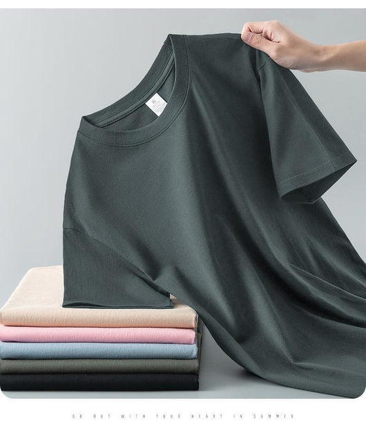 Light gray short-sleeve t-shirt with a round neck, held up to show its smooth fabric. A stack of folded t-shirts in various colors is visible in the background. - Image 29