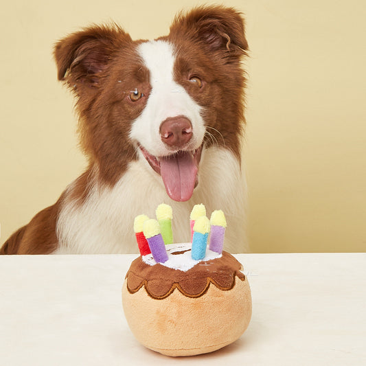 Plush pet birthday cake toy with colorful candles, featuring brown cake layers and white frosting.