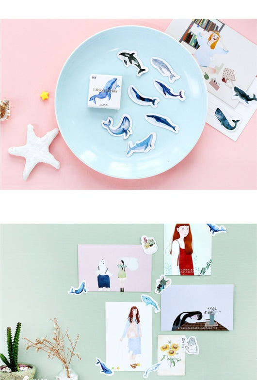 Box of 'Lifelog sticker' whale stickers with various blue whale designs scattered on a light blue plate. - Image 8