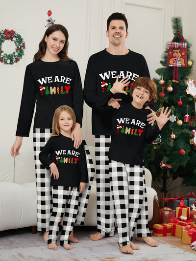 Family of four wearing matching black long-sleeve pajamas with "WE ARE FAMILY" text and black and white plaid bottoms. - Image 5