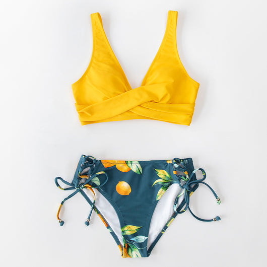Woman in a yellow front cross lace-up bikini top and dark blue orange fruit print side-tie bottoms on a beach. - Image 21