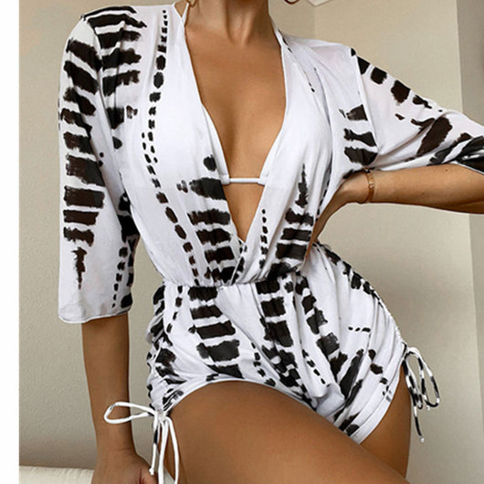 Woman wearing a white and black tie-dye beach cover-up romper with a deep V-neck and drawstring sides. - Image 4