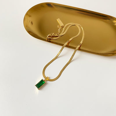 Gold hoop earrings with rectangular emerald green zircon pendants, displayed on a light beige fabric. - Image 12