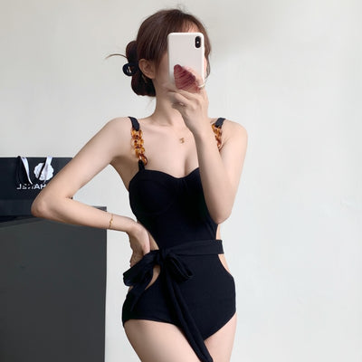 Black ribbed one-piece swimsuit with sweetheart neckline, chain-link shoulder strap, side cut-outs, and self-tie waist.