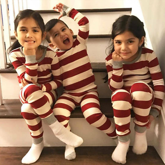 Family of four in matching red and white striped Christmas pajamas, sitting on a white rug with holiday decor. - Image 10