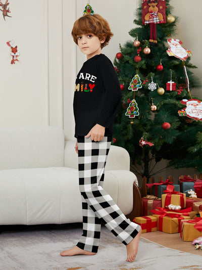 Family of four wearing matching black long-sleeve pajamas with "WE ARE FAMILY" text and black and white plaid bottoms. - Image 10