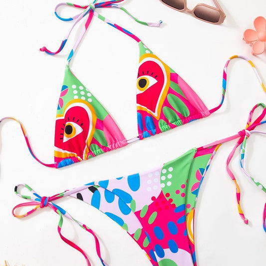 Women's vibrant abstract eye print bikini with triangle top and tie-side bottoms, featuring pink, green, and blue.
