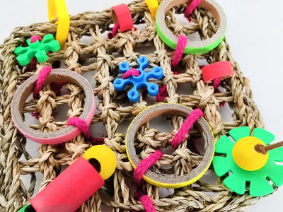 Colorful parrot bite toy with a woven grass mat, yellow plastic hangers, and various red, green, blue, and brown chewable components. - Image 4