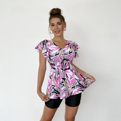 Woman in a blue, black, and white floral print swim top with flutter sleeves and black swim shorts. - Image 2