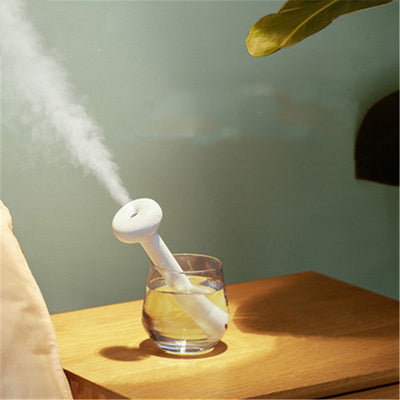 Clear bottle-shaped USB humidifier with a white donut-style top, emitting a stream of cool mist on a wooden table. - Image 4