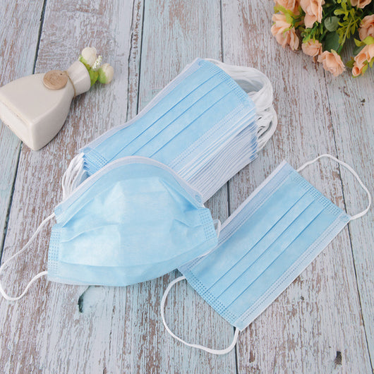 Stack of pink disposable non-woven face masks, with one unfolded and one folded, on a light wood surface. - Image 2