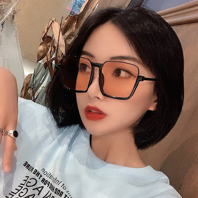 Retro square sunglasses with black frames and brown lenses held by a hand with patterned nails and a gold ring. - Image 2