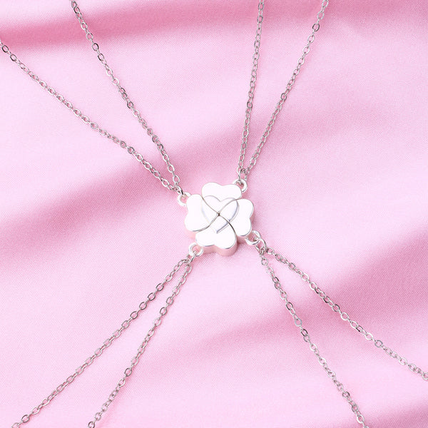 Four silver-colored necklaces, each with a half-heart charm that forms a four-leaf clover when combined, on pink satin. - Image 3