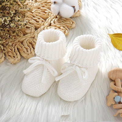 Pink knitted infant toddler shoes with cute bowknots and elastic bands, displayed on a soft white rug.