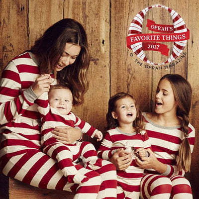 Family of four in matching red and white striped Christmas pajamas, sitting on a white rug with holiday decor. - Image 3