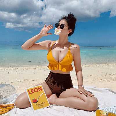 Woman in a yellow ruffled bikini top and dark brown high-waisted bottoms sitting on a beach. - Image 3