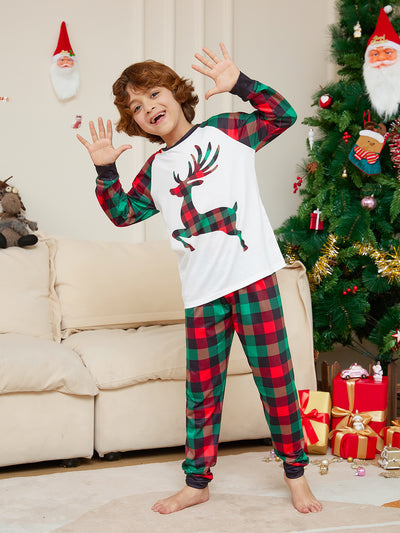 Two children in matching red and green plaid Christmas pajamas with a reindeer graphic, standing by a Christmas tree. - Image 8