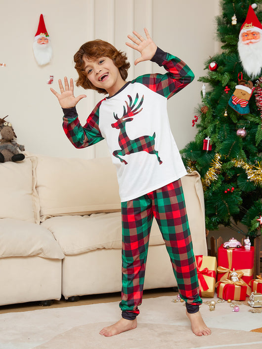 Two children in matching red and green plaid Christmas pajamas with a reindeer graphic, standing by a Christmas tree. - Image 8