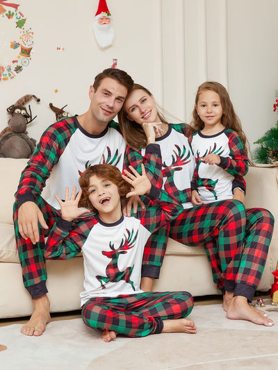 Two children in matching red and green plaid Christmas pajamas with a reindeer graphic, standing by a Christmas tree. - Image 5